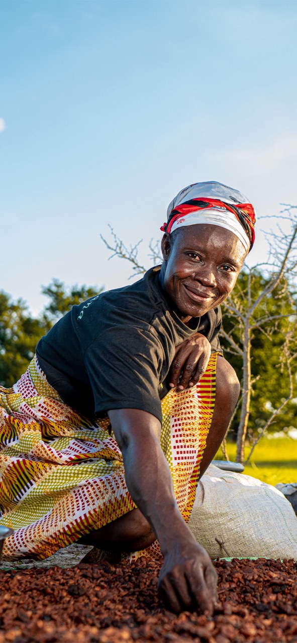 Ghanaian farmer smiling working with cocoa beans outdoors in traditional clothing