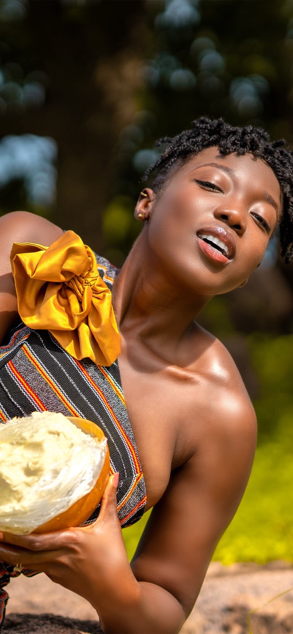 Woman holding shea butter product outdoors in natural sunlight with vibrant Ghanaian cloth