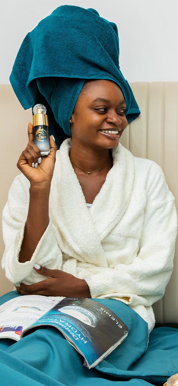 Woman in turquoise towel holding luxury skincare serum bottle with confidence