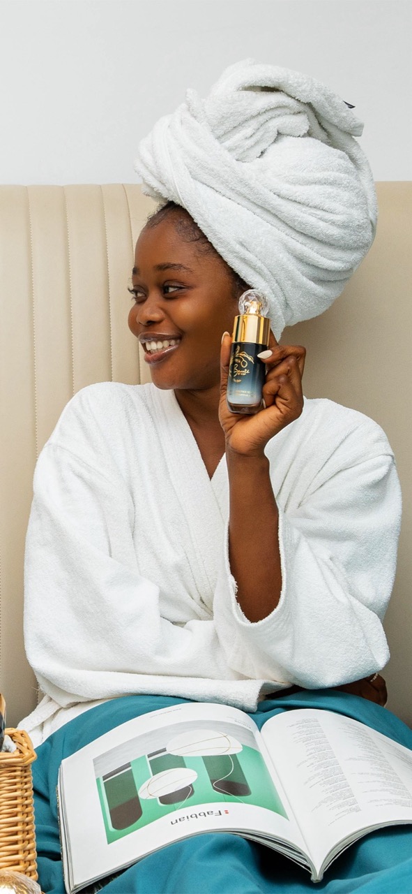 Woman in white towel wrap holding gold-capped skincare serum bottle for beauty routine
