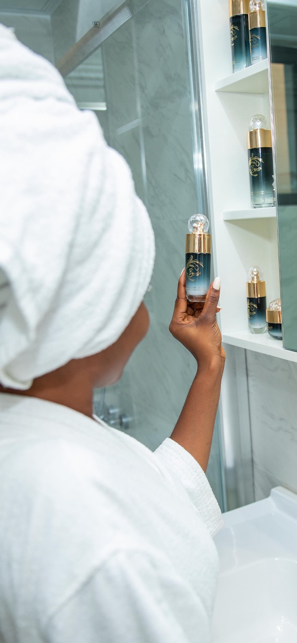 Woman's hand reaching for luxury serum bottle on bathroom mirror shelf